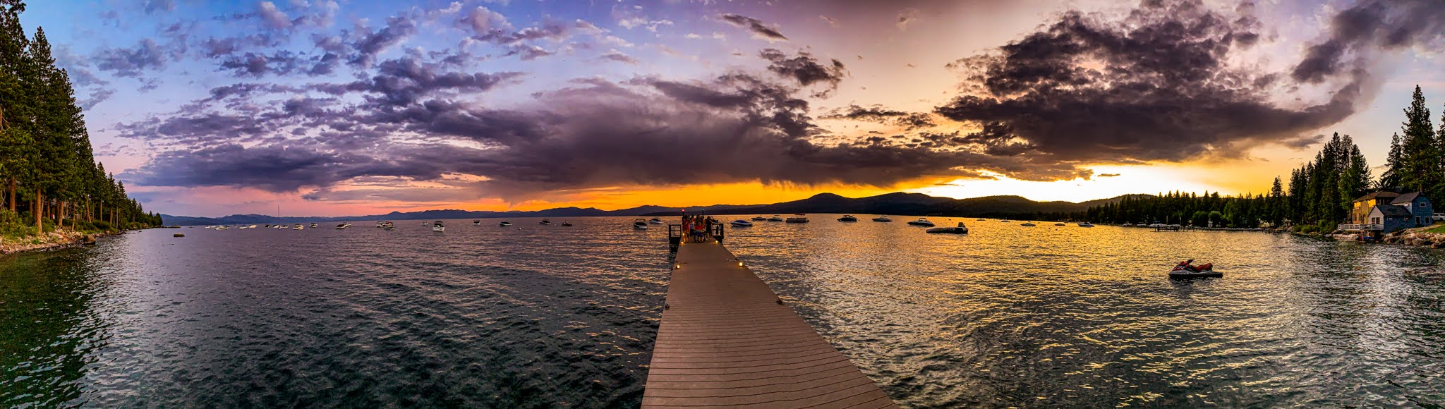 Panoramic sunset over Lake Tahoe, with boats moored near a dock and storm clouds catching the last light